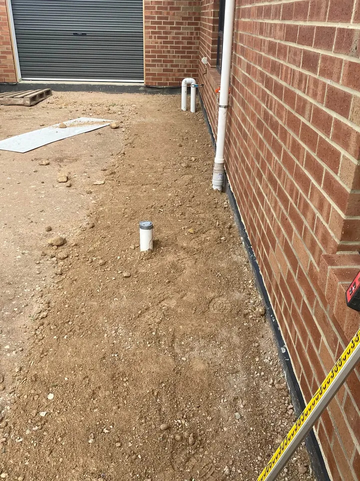 Dirt beside a red brick wall with a pipe in the corner