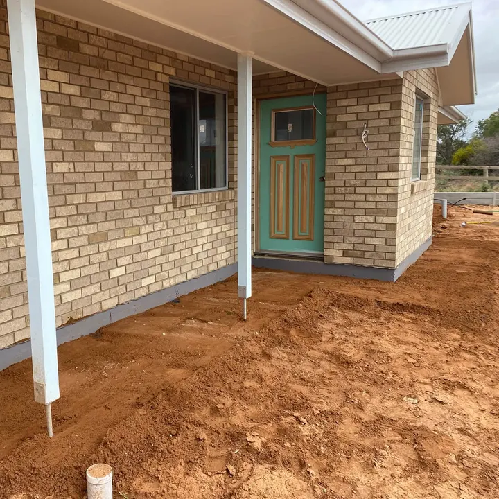 Red dirt out the front of a brick house with a teal door
