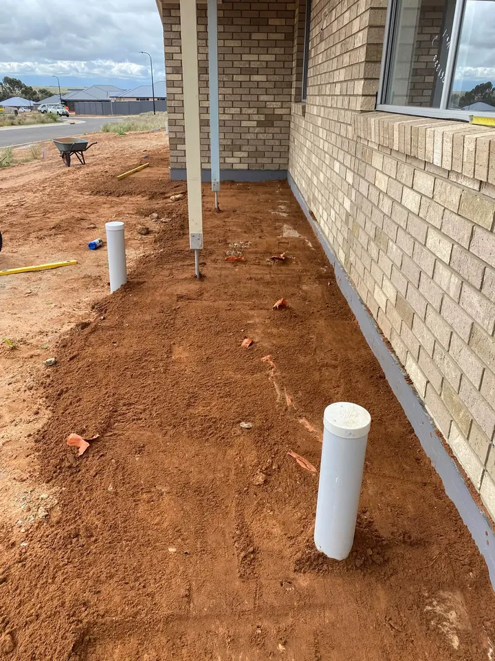 Red dirt beside a cream brick wall, a white pipe standing up