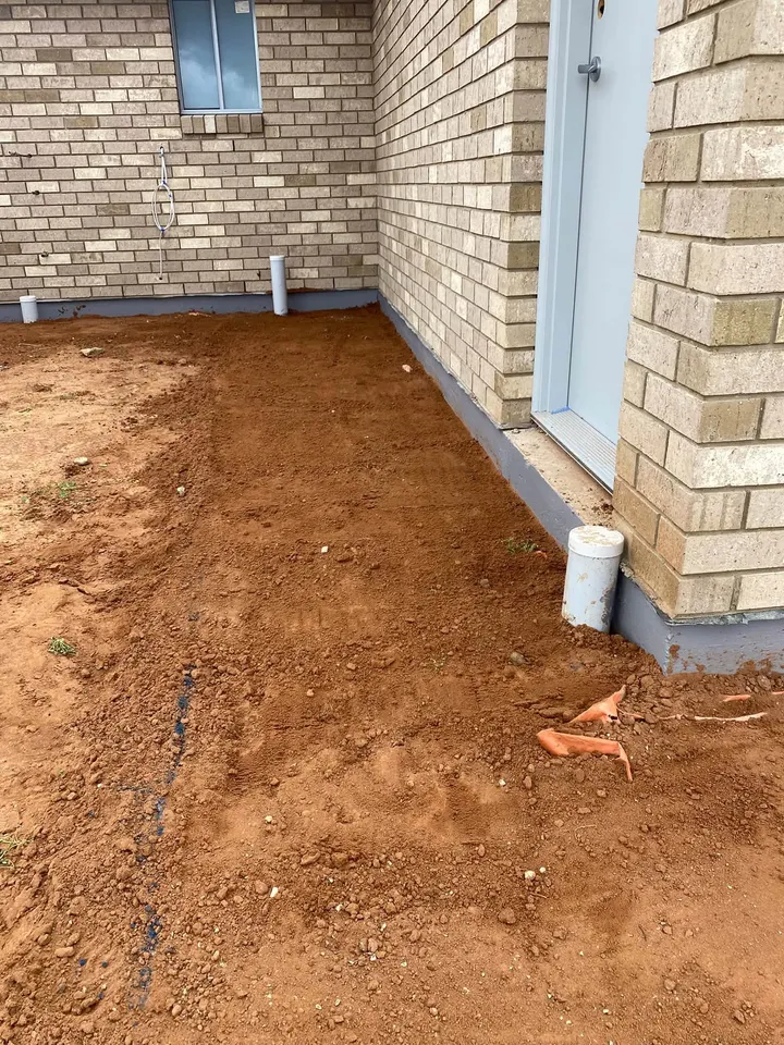 Red dirt in the corner of a cream brick house