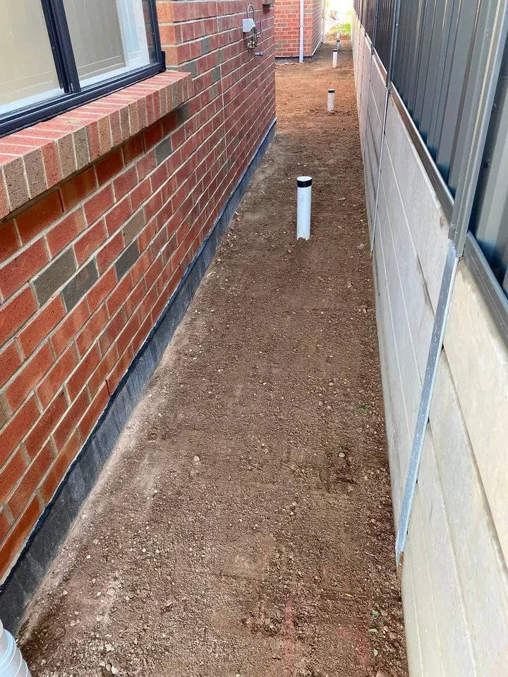 A side path of dirt between a red brick wall and a fence