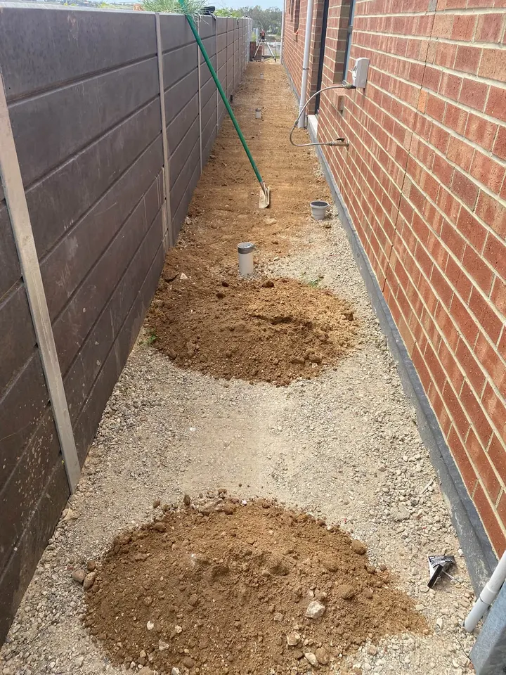 Crushed rock and two piles of dirt along a red brick wall