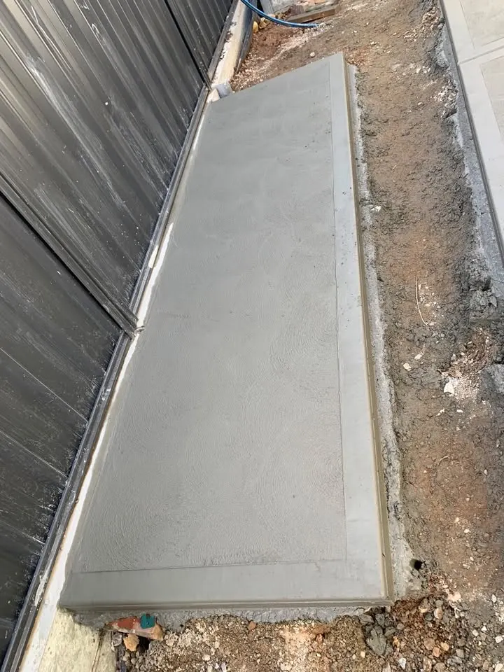 A concrete path beside a dark fence with dirt along its edge