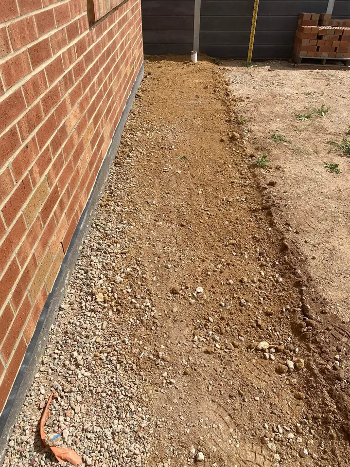 Dirt down a side path with crushed rock going in along the red brick wall