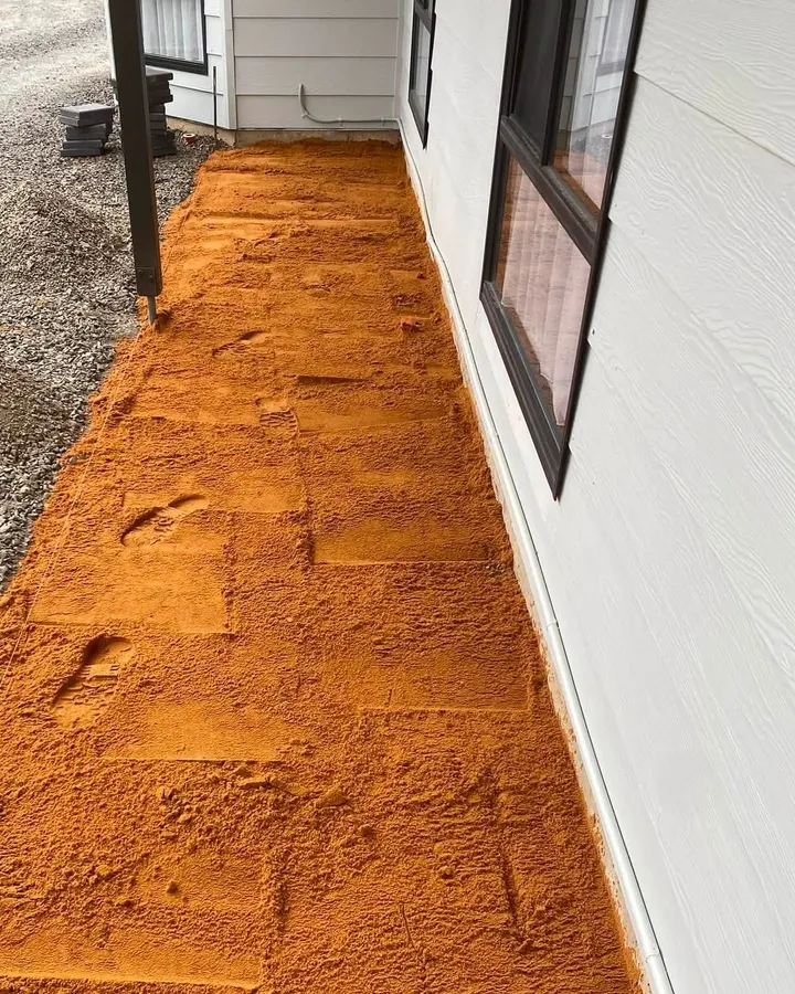 Orange sand laid along the wall of a house, gravel to the left