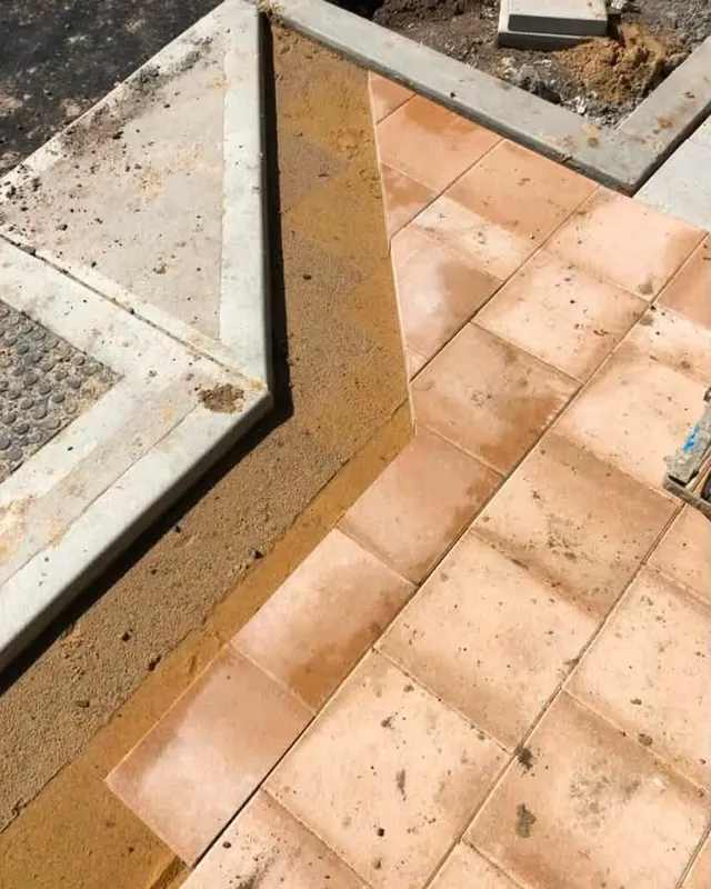Terracotta coloured pavers meeting a concrete edge and tactile ground indicators