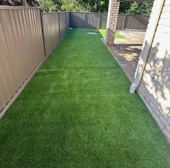Artificial turf laid down a narrow side path between a fence and a brick wall